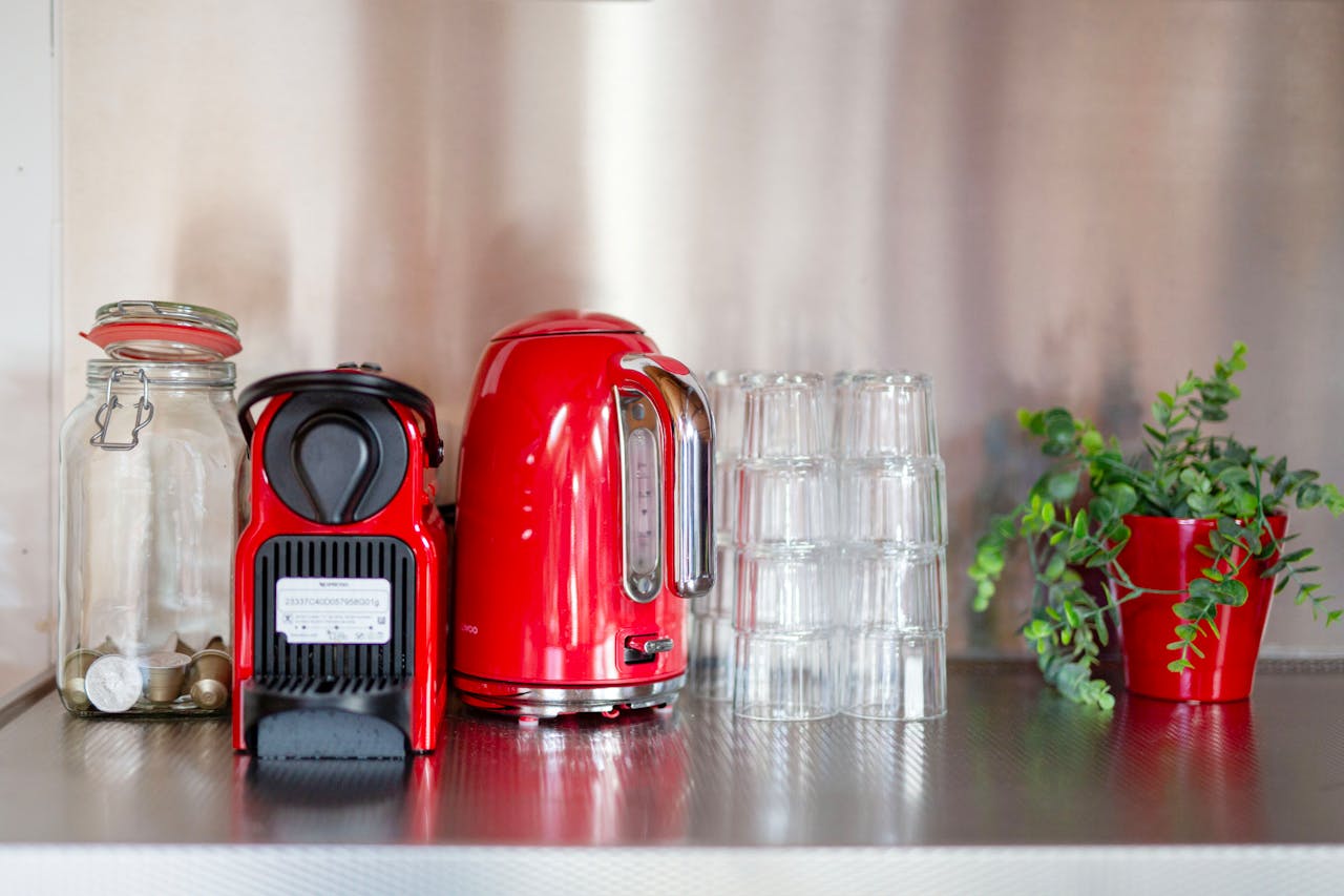 Stylish kitchen set-up with red appliances and greenery on a steel counter. Perfect for coffee lovers.