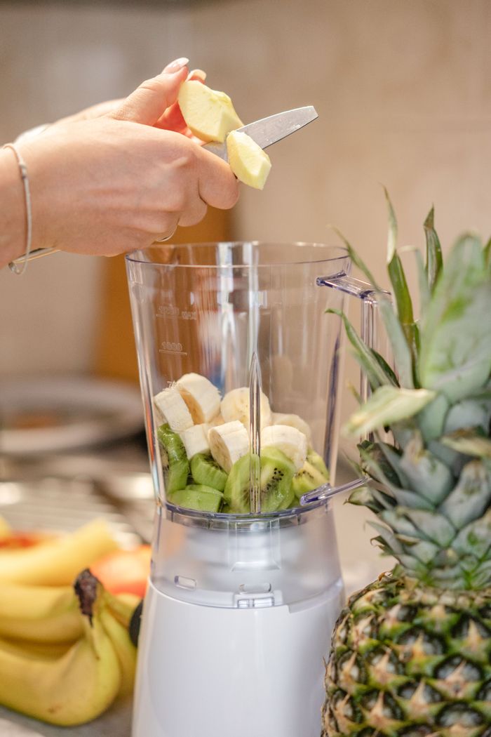 journey Close-up of hands preparing fresh fruit smoothie with blender, featuring bananas, kiwi, and pineapple.