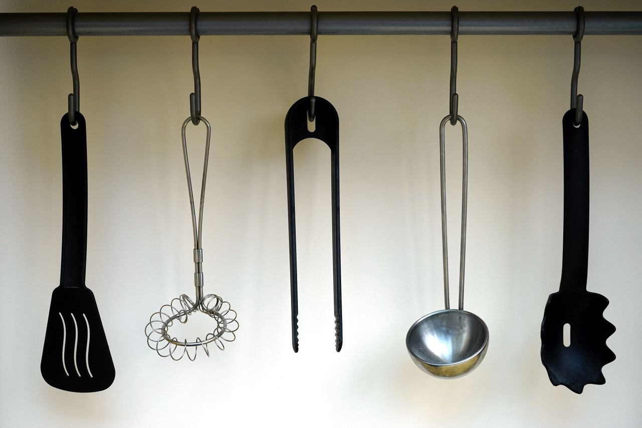 category-03 A set of stainless steel and plastic kitchen utensils hanging on a rail.